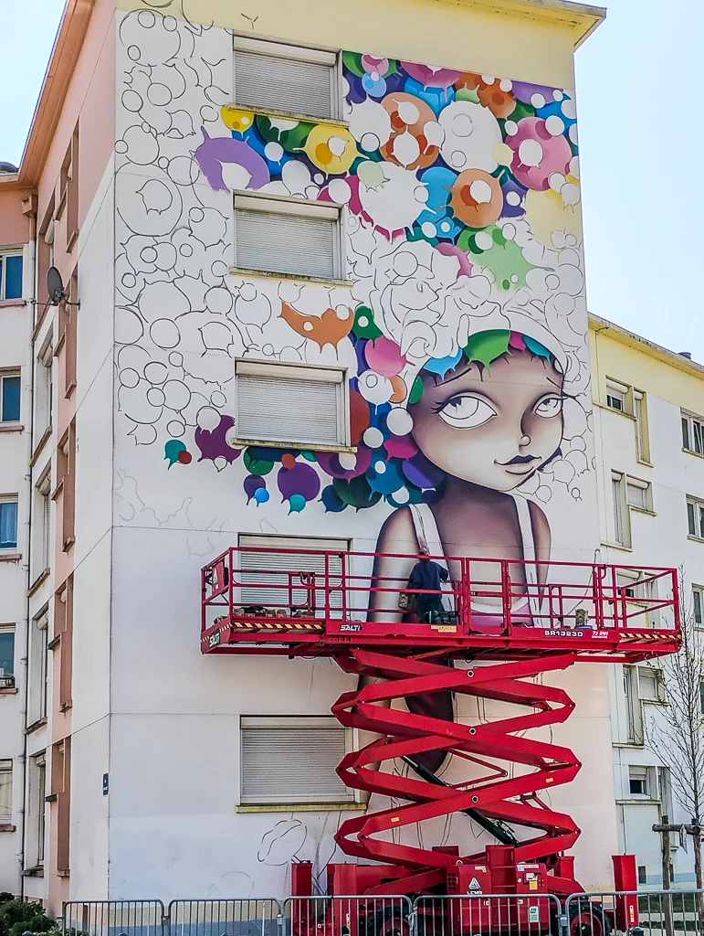 Vinie, artiste de street-art, sur sa nacelle en train de travailler sa fresque